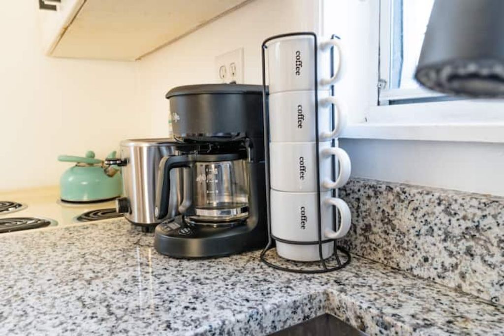 En kaffemaskine og en holder til kaffekopper på en køkkenbordplade.