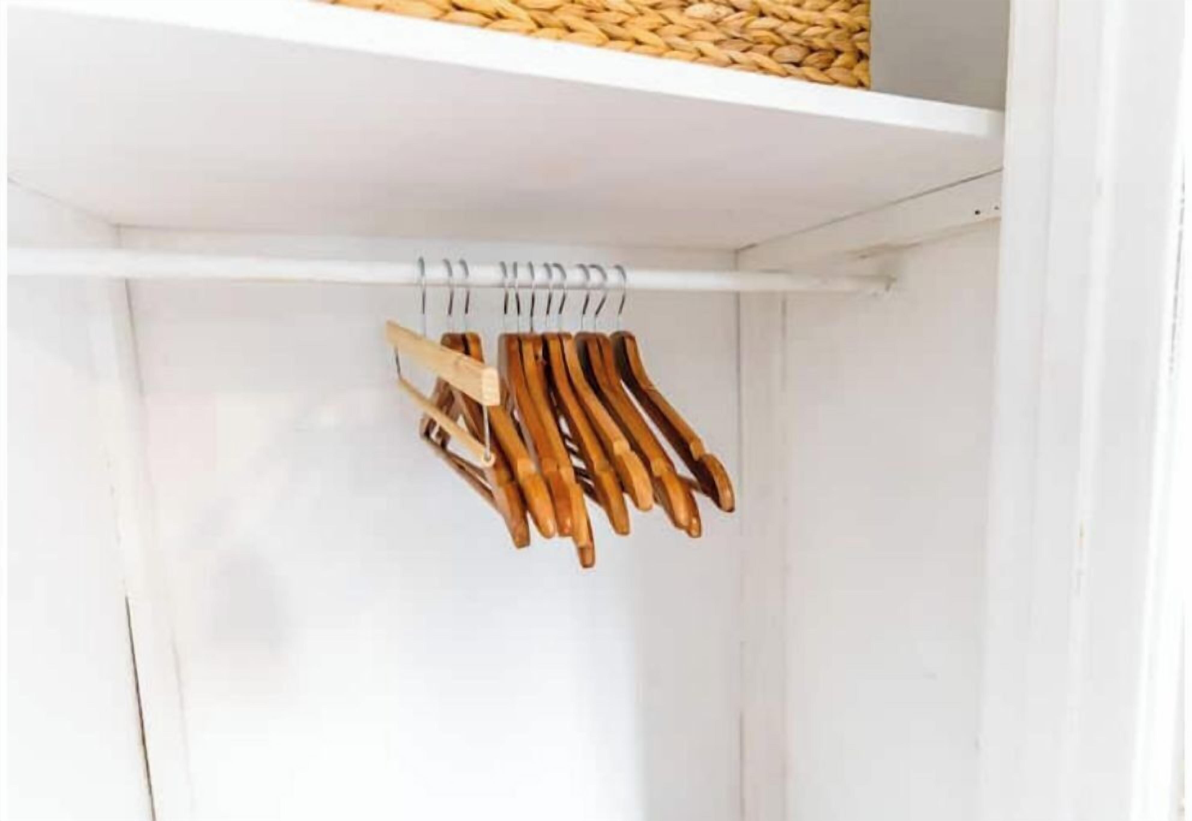 A white closet with a wooden hanger rod and a woven basket on top.