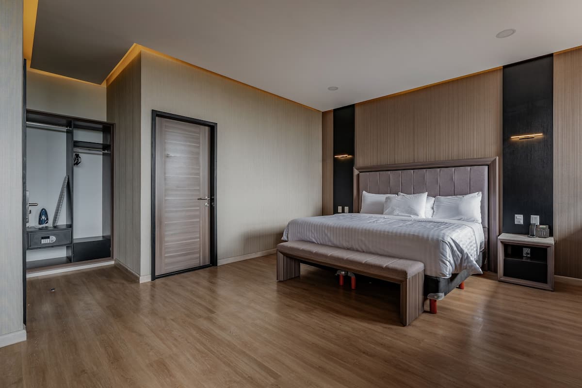 A modern bedroom with a large bed, bedside tables, a bench, a wardrobe, and a mirror.