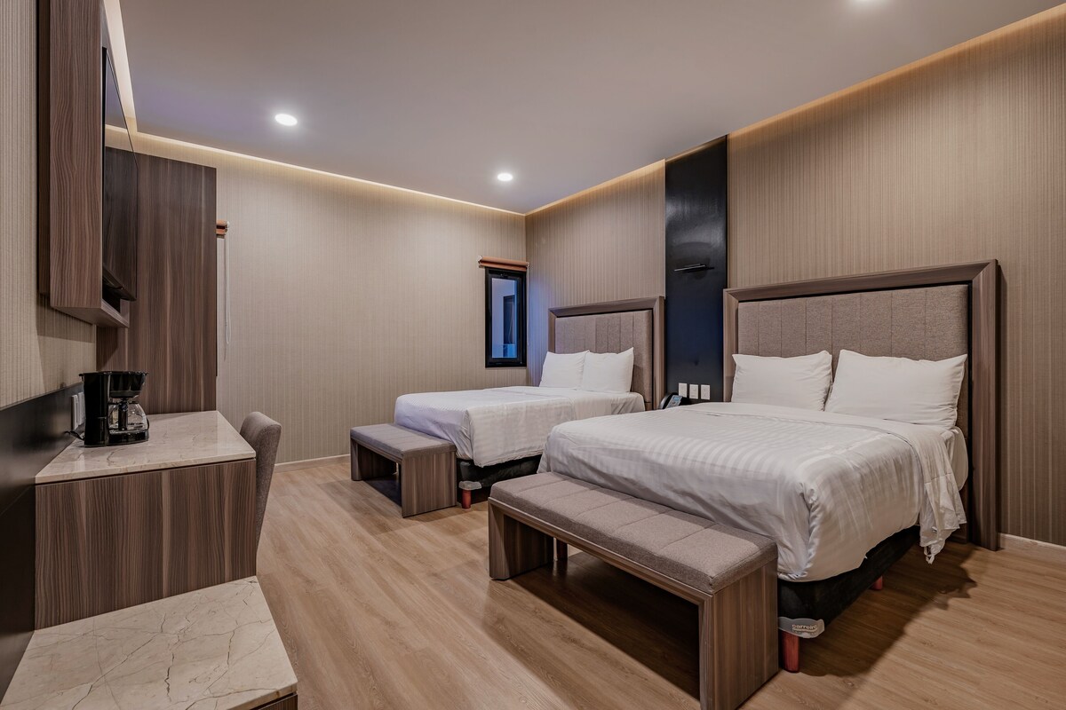 Une chambre d’hôtel avec deux lits, un bureau, une banquette et une machine à café.