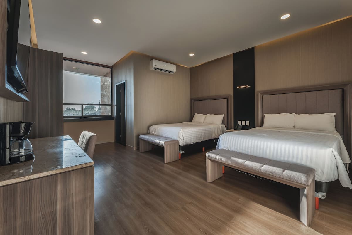 A modern hotel room with a wooden floor, two single beds, a large bed, a bench, a desk with a coffee maker, and a large window.
