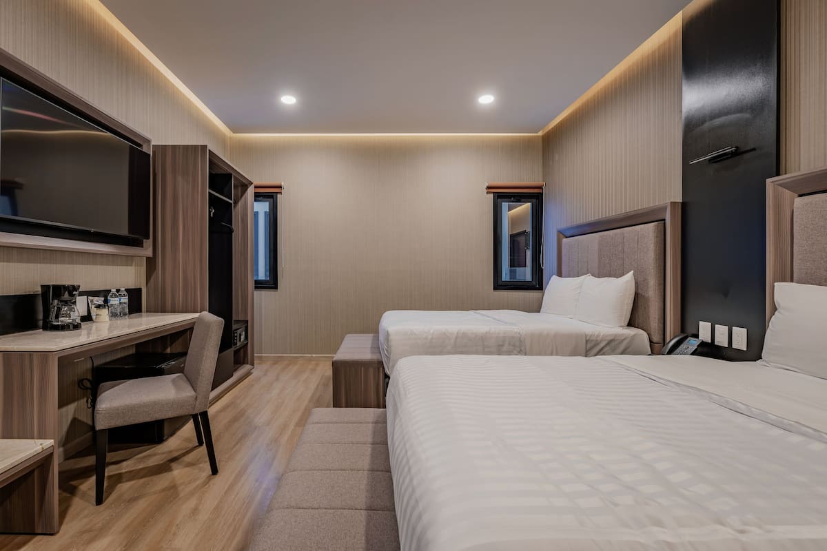 A modern hotel room with a desk, two beds, a TV, and a wardrobe.