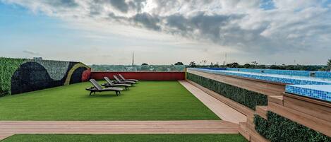 A rooftop garden with artificial grass, lounge chairs, and a pool area.