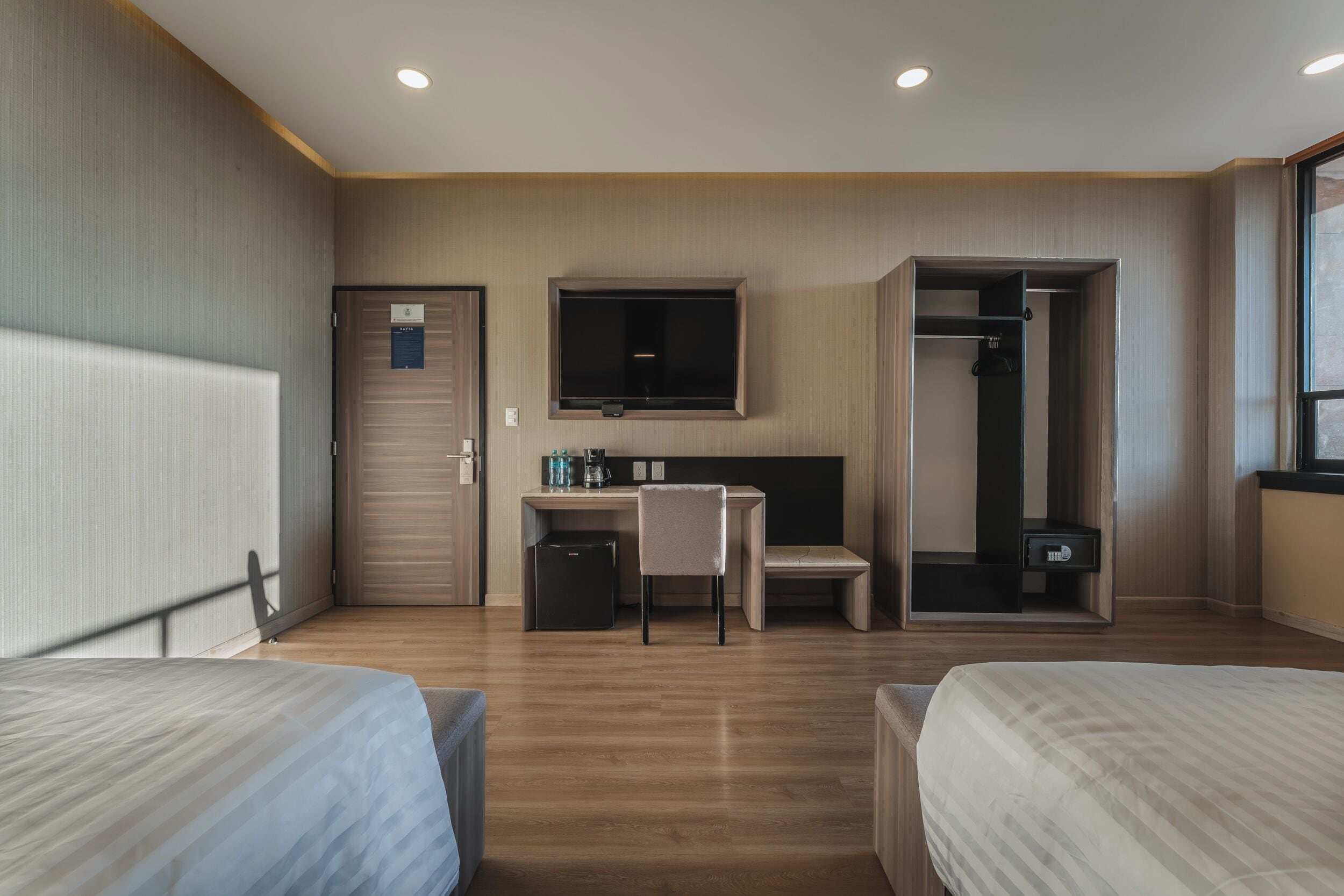 Una habitación de hotel con dos camas, un escritorio con silla, televisor, armario y una pequeña kitchenette.