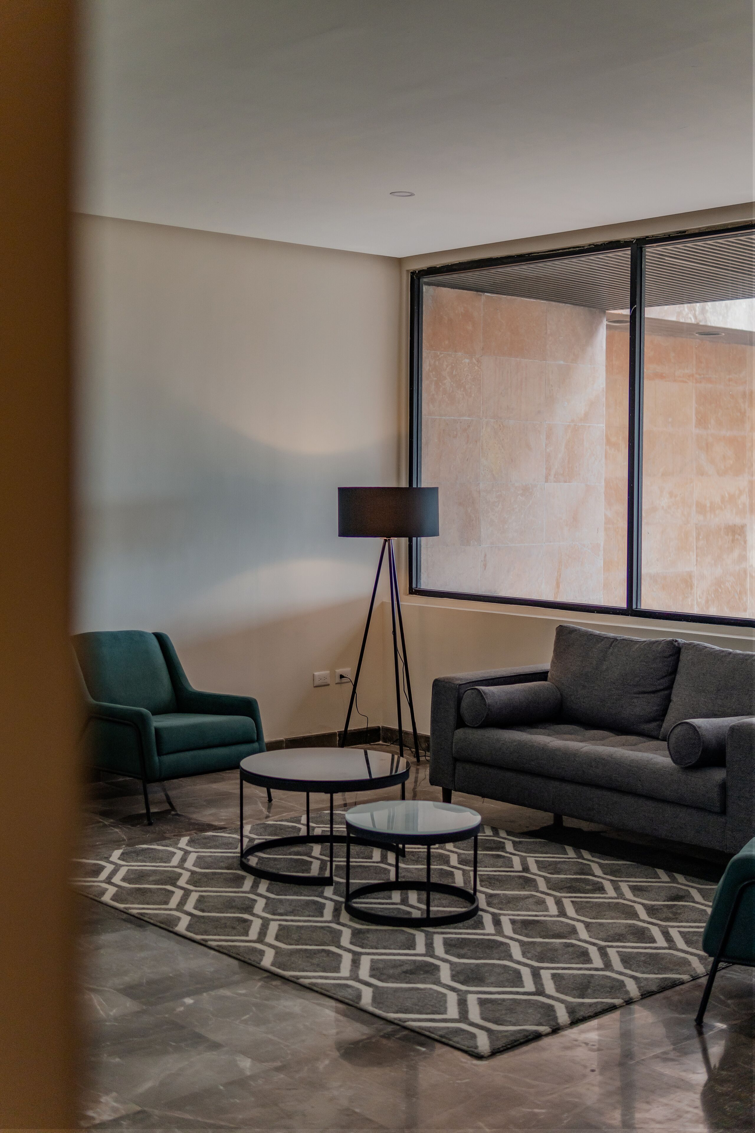 Una sala de estar moderna con un sofá, dos sillones, una lámpara de pie y un tapete estampado.
