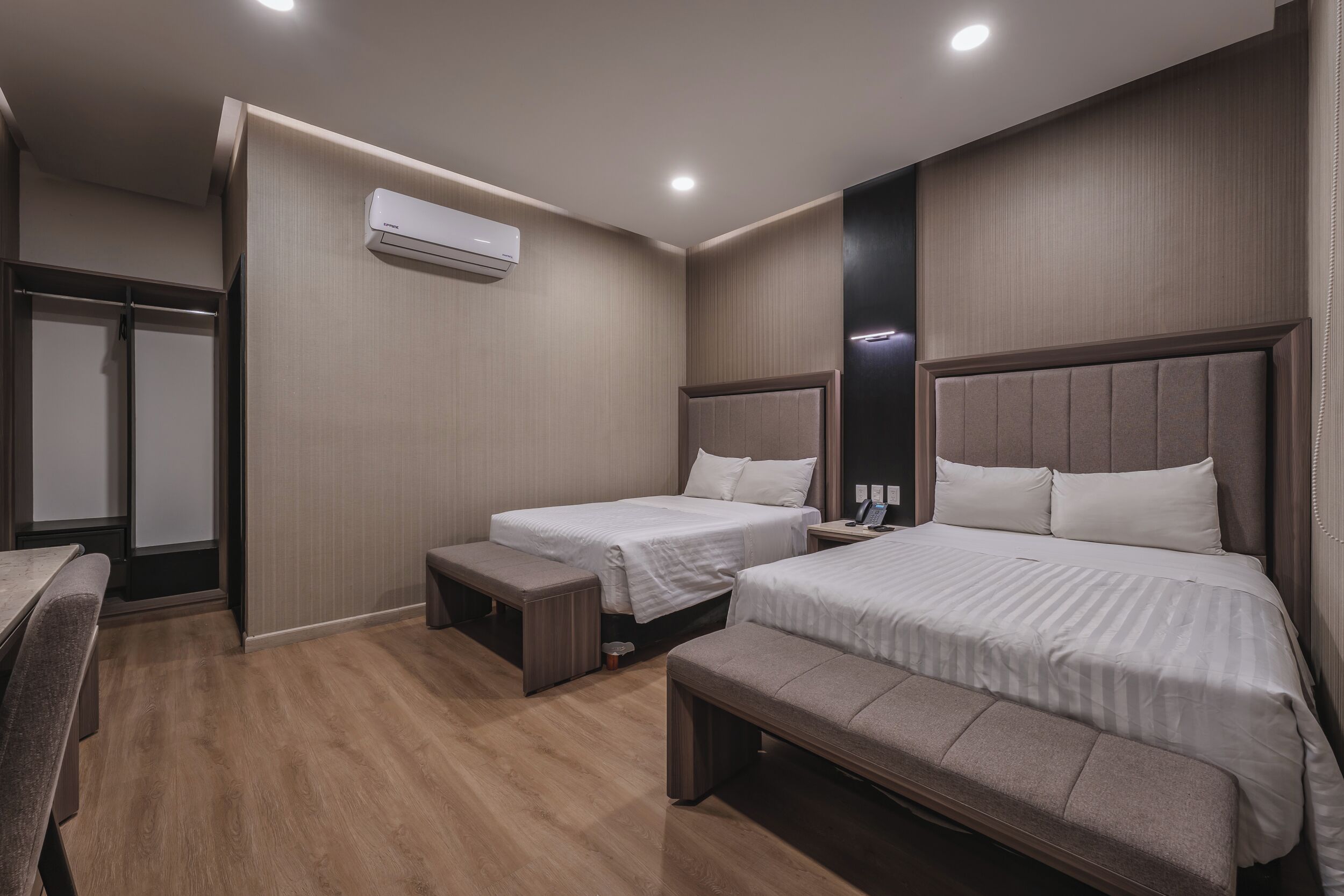 Habitación de hotel con dos camas, un banco, un escritorio y un armario.