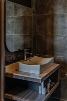 Un baño moderno con un lavamanos grande y curvo, un espejo y paredes oscuras con textura.