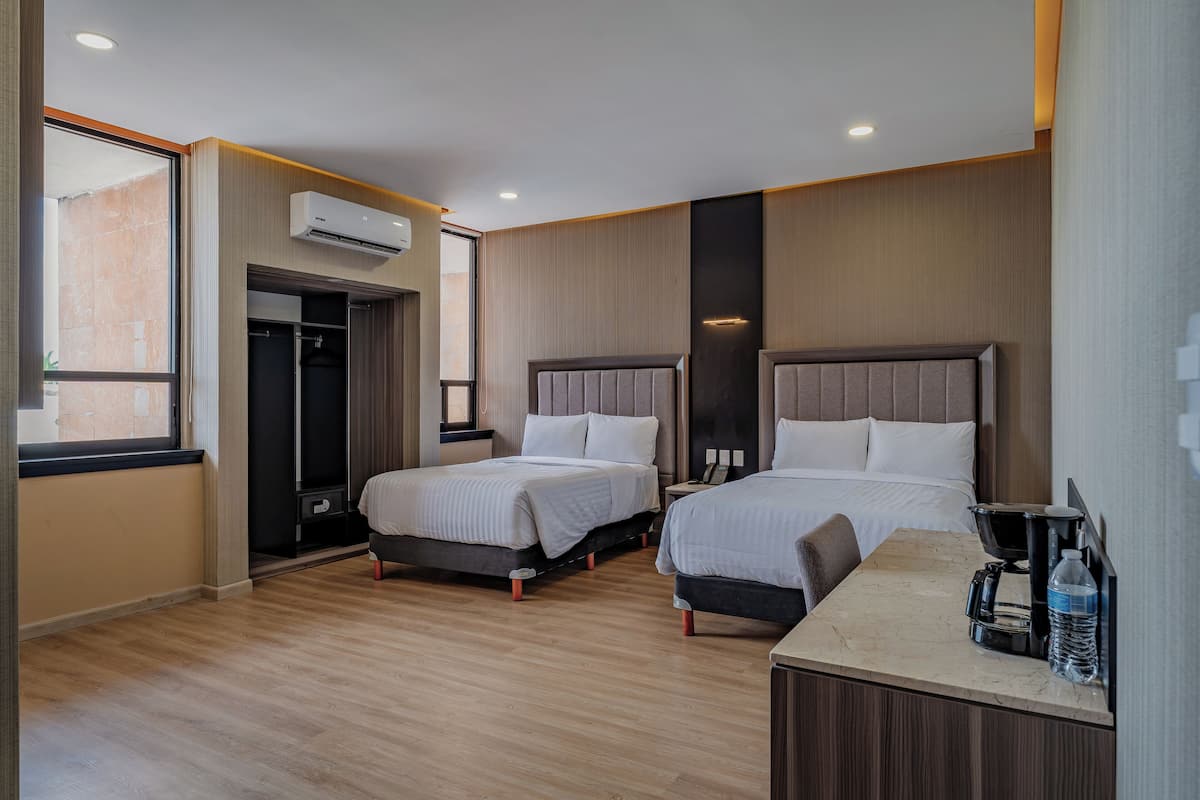 A hotel room with two beds, a desk with a coffee maker, and an air conditioning unit.