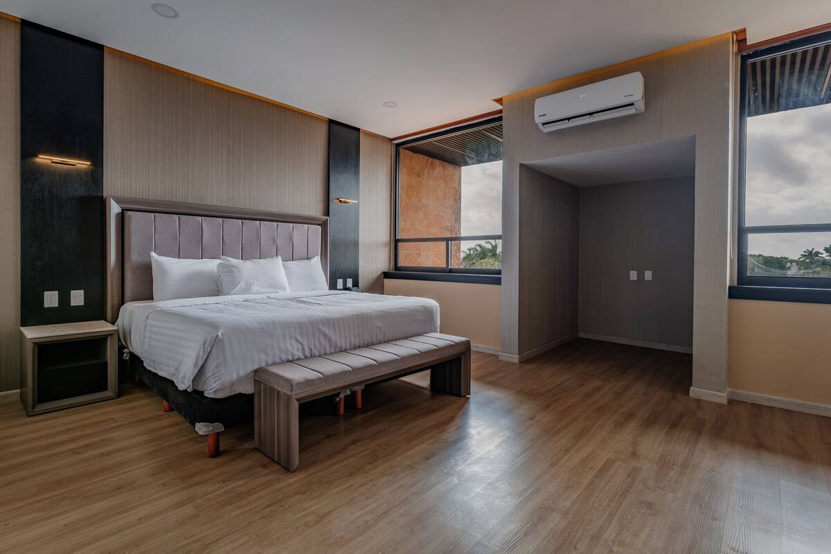 A modern bedroom with a large bed, built-in bench, and a view through a window.