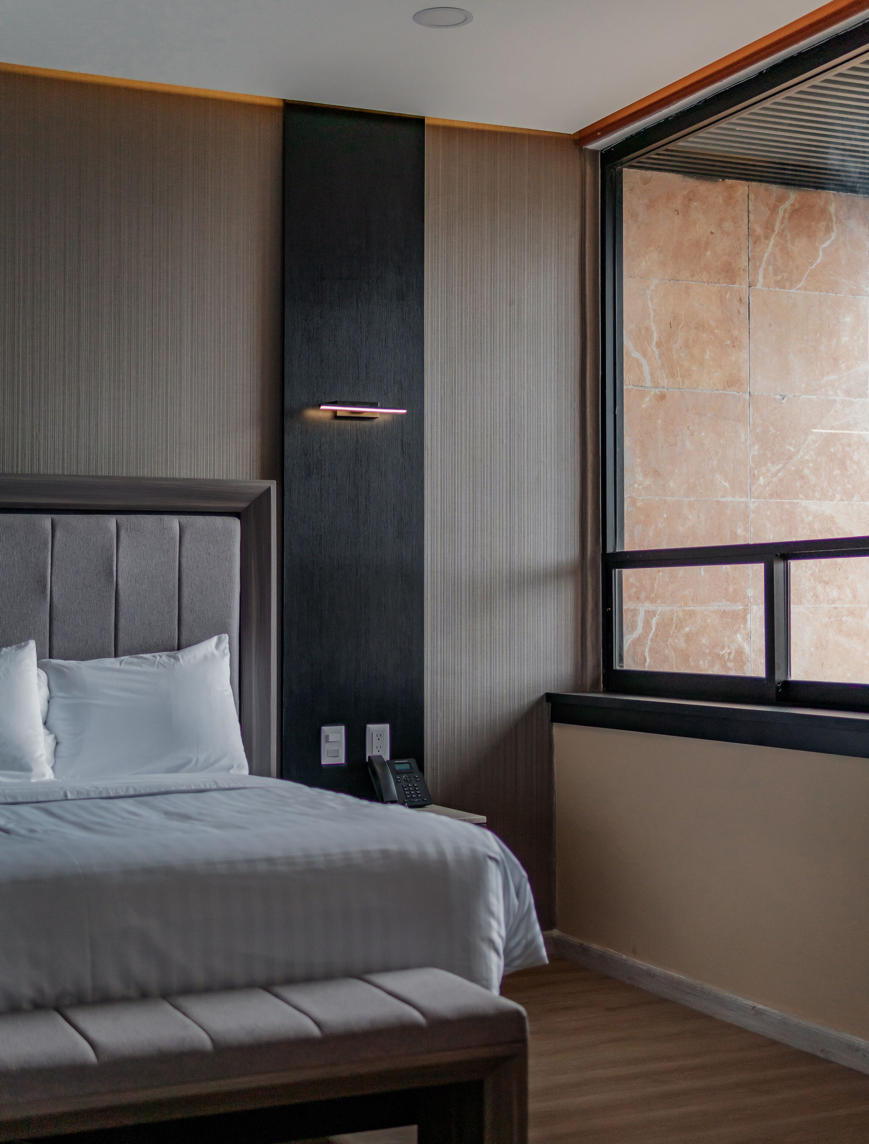 A modern hotel room with a large bed, a bedside telephone, and a window with a stone view.