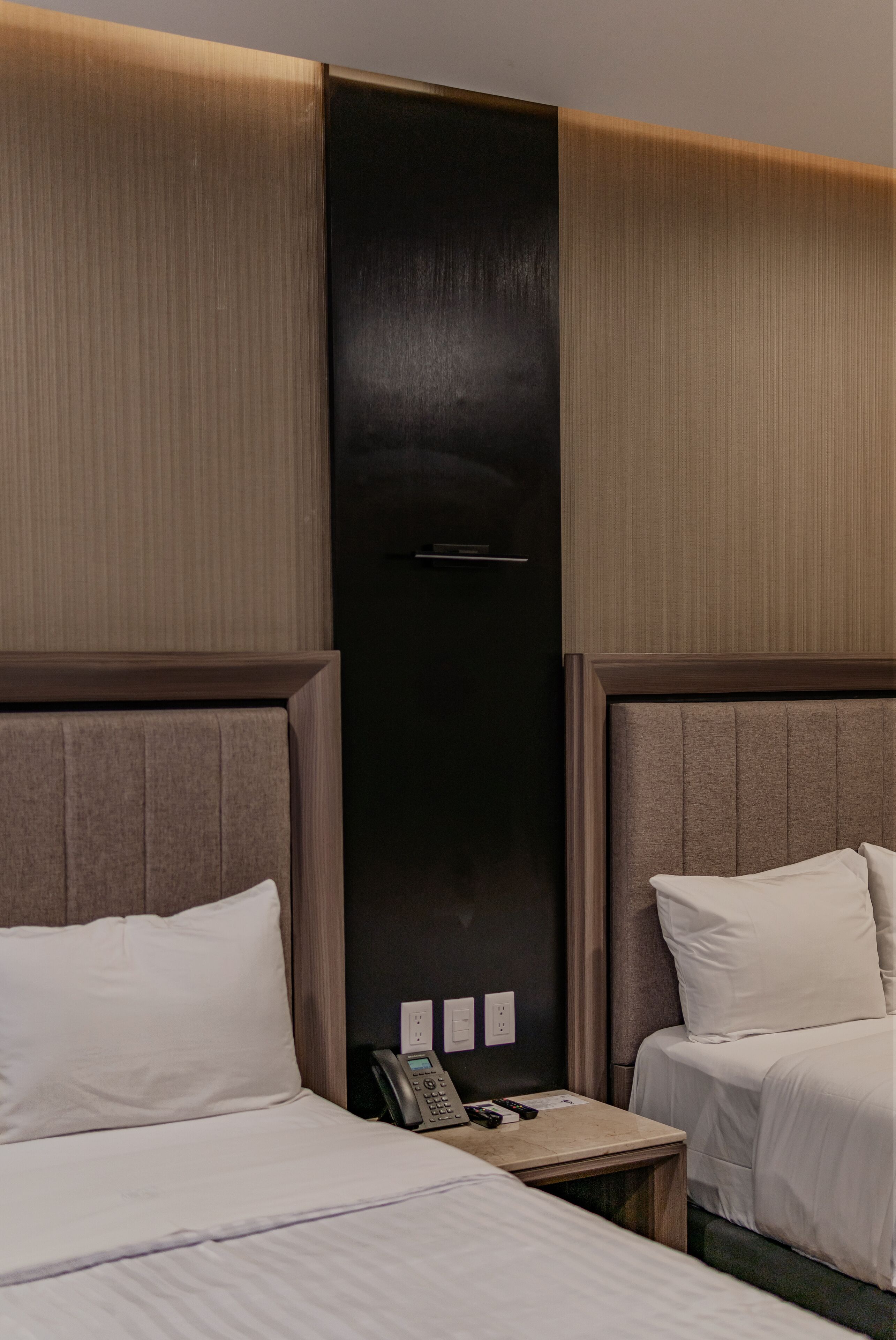 A hotel room with two beds, a bedside table with a phone, and a door with a handle.