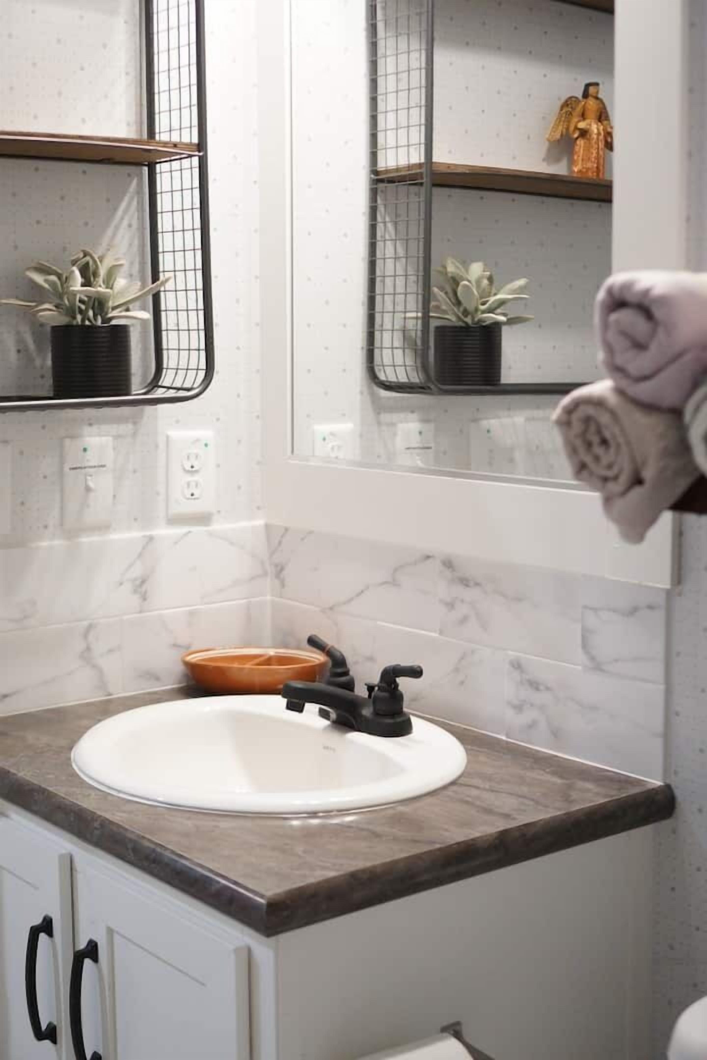 A bathroom with a white sink, black faucet, marble backsplash, and a towel rack with a rolled towel.