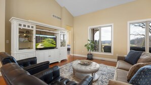 Ein Wohnzimmer mit großem Flachbildfernseher, Ledersofas, einem Couchtisch und Blick auf einen Golfplatz durch ein Fenster.