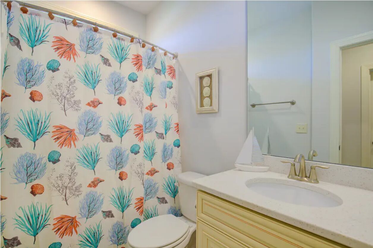 A bathroom with a shower curtain featuring a leaf pattern, a white sink, a mirror, and a toilet.