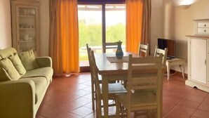 A cozy living room with a green sofa, wooden dining table, and chairs. There is a cabinet and a TV on the right side. - Villa Claudia, private pool (Stintino)