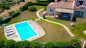 A two-story house with a swimming pool, a patio with chairs, and a well-maintained garden. - Villa Claudia, private pool (Stintino)
