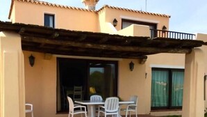 A covered patio with a table and chairs, a grassy lawn, and a building with a tiled roof and windows. - Villa Claudia, private pool (Stintino)