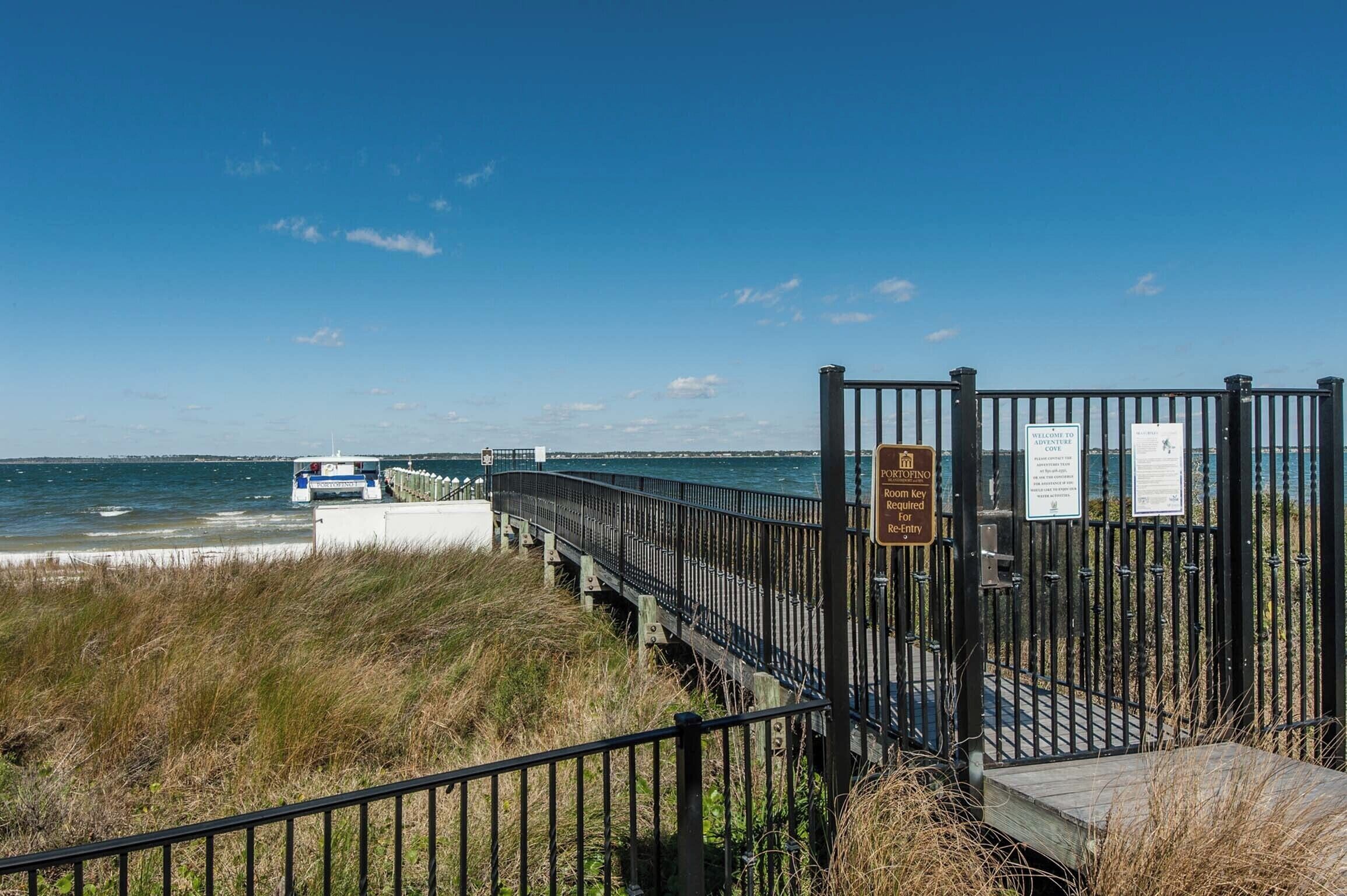 A coastal walkway with a metal railing, a sign indicating a key entry point, and a view of the sea.