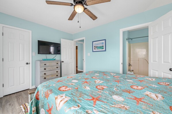 Un dormitorio con cama, cómoda, televisor y ventilador de techo.