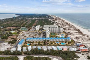 Vista aérea de un complejo hotelero frente al mar, con varias construcciones, una playa y una torre de agua grande.