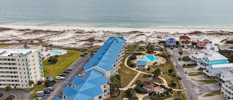 A resort with a long building with blue roofs, a pool, and a beach view.