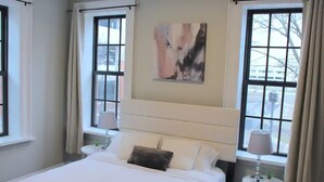 Ein Hotelzimmer mit einem großen Bett, zwei Nachttischen, einem Vorhangfenster und einem Bild an der Wand.