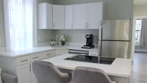 Eine moderne Küche mit weißen Schränken, einem Edelstahlkühlschrank, einer Kaffeemaschine und zwei grauen Barhocker.
