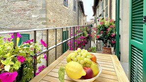 Un balcón con una mesa de madera que sostiene un cuenco de frutas y flores.
