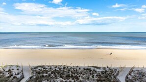 Una spiaggia con una battigia sabbiosa, cielo sereno e una persona che cammina lungo la riva.