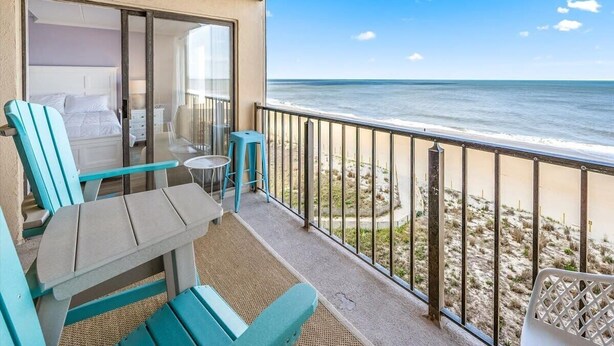 Un balcone con vista sull'oceano, un letto e un tavolo con sedie.