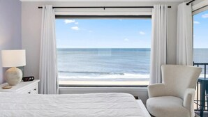 Una camera d'albergo con un letto, una sedia, un comodino con una lampada e vista sull'oceano.