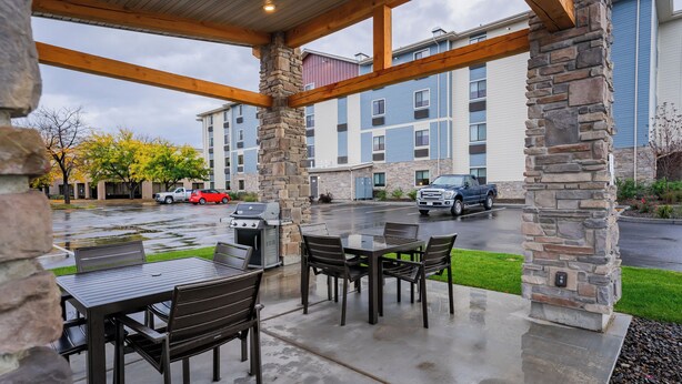 An outdoor patio with stone pillars, a covered seating area, and a view of a multi-story building with parked cars. - My Place Hotel-Boise/Nampa, ID-Idaho Center (Nampa)