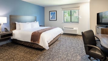 A hotel room with a large bed, a desk with a chair, a television, and a window with blinds.