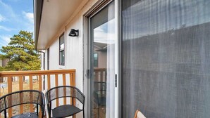 Ein Balkon mit zwei schwarzen Stühlen, einem Holzboden und einer Schiebetür zu einem Innenraum.