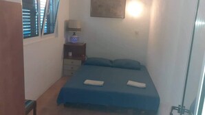 A small, single-bed room with a blue bedspread, a bedside table with a lamp, and a window with blinds. - Apartments Kamaki - Two Bedroom Apartment with Balcony and Sea View (Gradac)
