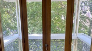 En trädör med en metalgreb, der fører til en udendørs balkon med gelænder og udsigt over grøntområde.