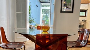 Et moderne spiseområde med et glasbord og metalstole, udsigt til det fri og et køkken i baggrunden.