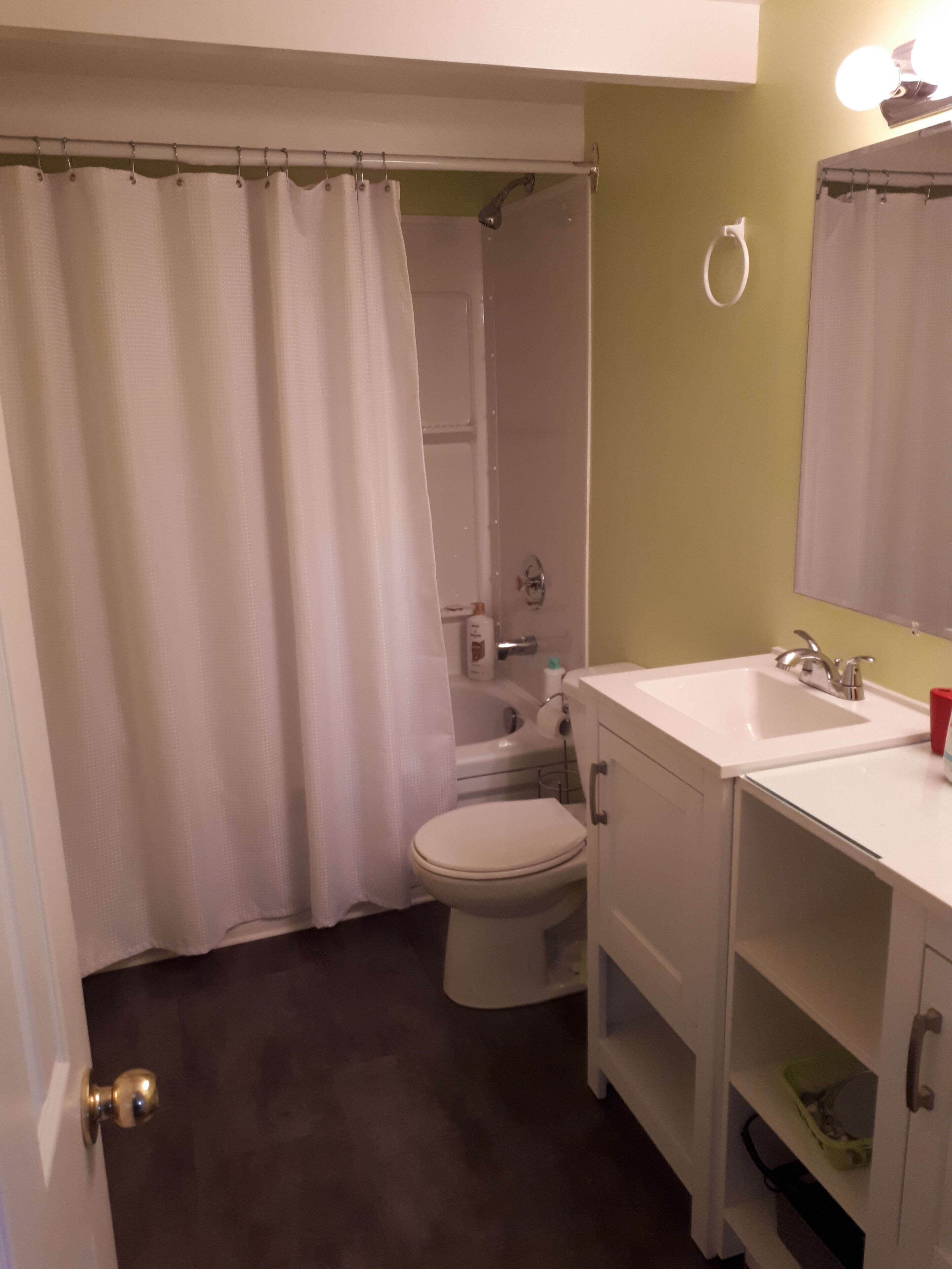 A bathroom with a shower curtain, toilet, sink, and mirror.