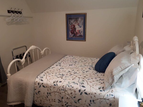 A bedroom with a bed, a bedside table, a wall-mounted picture, and a coat rack. - Lands End Vacation Home (Twillingate)