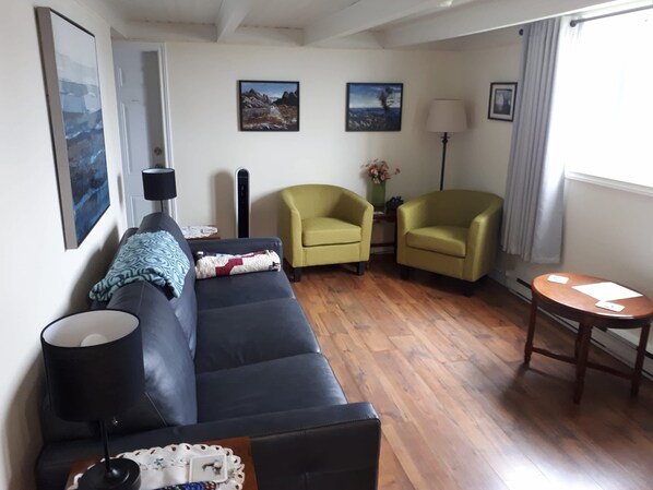 A living room with a black sofa, two green armchairs, a small wooden table, and a floor lamp. - Lands End Vacation Home (Twillingate)