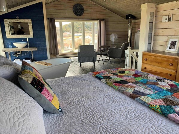 Ein Schlafzimmer mit einem großen Bett, einem Fenster mit Vorhängen, einem Waschbecken, einem Stuhl und einer Kommode.
