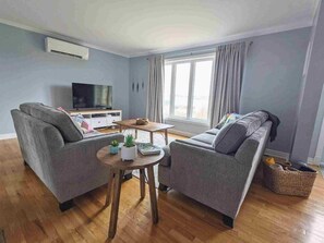 Ein Wohnzimmer mit zwei Sofas, einem Couchtisch, einem Fernseher und einem großen Fenster mit Vorhängen.