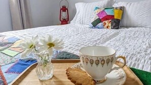 A neatly made bed with a white duvet, a colorful pillow, and a red lantern on the nightstand. - On the Rocks Overlooking the Sea (Twillingate)