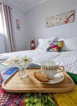 Ein ordentlich bezogenes Bett mit cremeweißer Bettdecke, einem farbenfrohen Kopfkissen und einer roten Laterne auf dem Nachttisch.