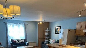 A modern kitchen with wooden flooring, a dining area with a table and chairs, a sofa, and a small bar area. - Jagged Rocks (Twillingate)