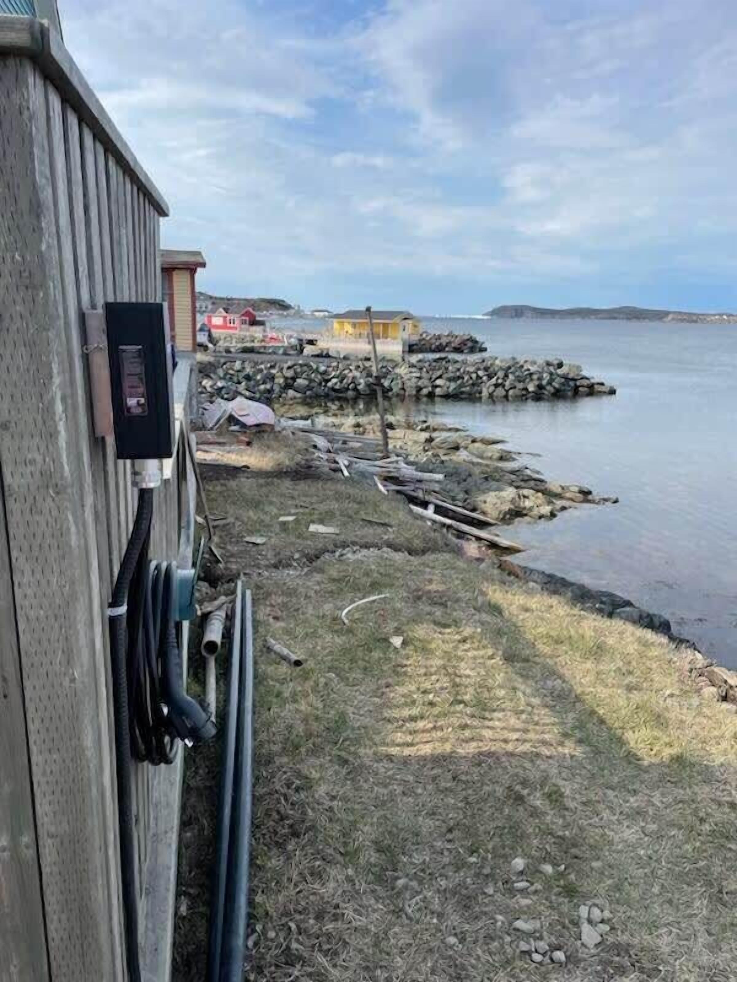 A waterfront property with a wooden building, a rocky breakwater, and a grassy area.