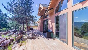 Une maison moderne dotée d’une terrasse en bois, de grandes fenêtres et offrant une vue sur les montagnes.