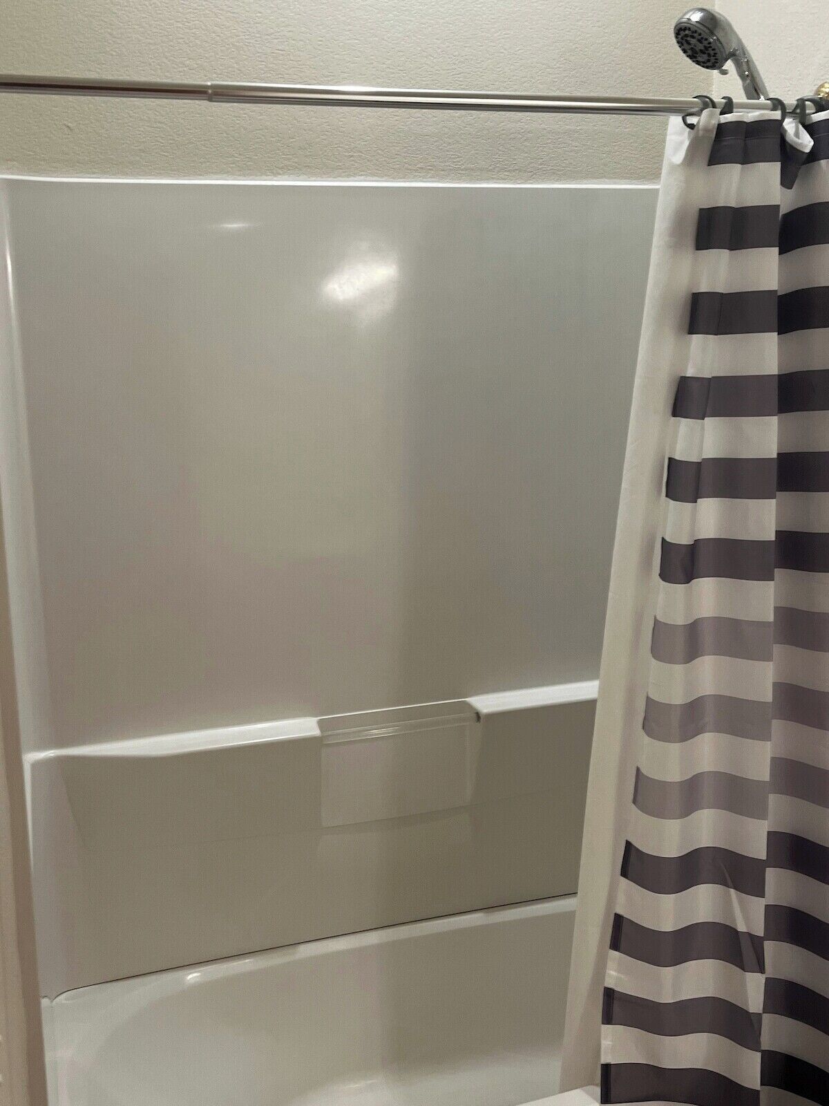 A shower area with a white bathtub and a striped shower curtain.