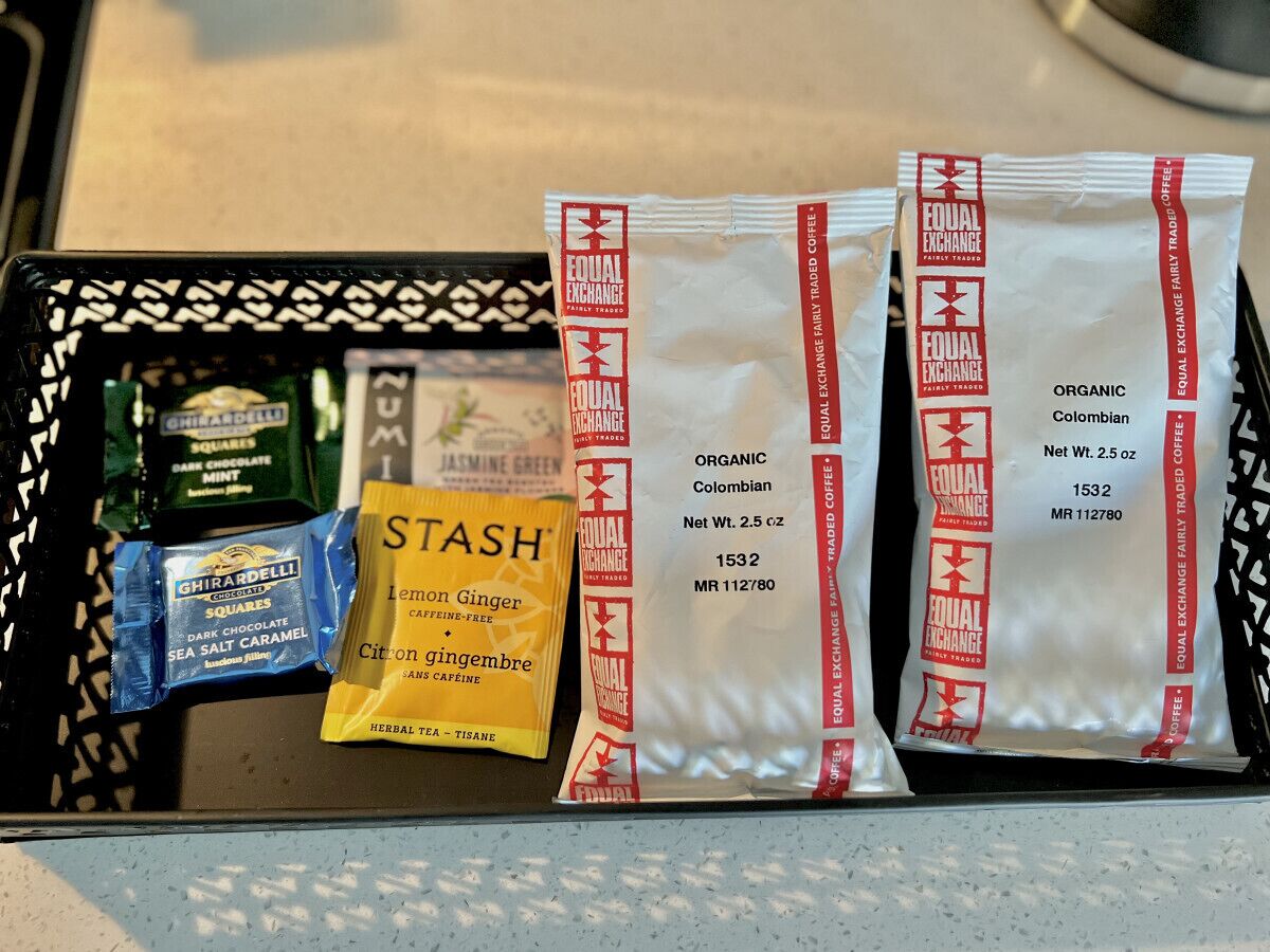 A tray with various food items including a pack of Equal Exchange fair trade coffee, a pack of Stash lemon ginger, a pack of Ghirardelli dark chocolate squares, and a pack of Ghirardelli sea salt caramel.