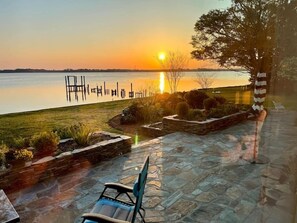 A patio with stone flooring, a chair, and a view of a lake at sunset. - Little piece of heaven in your own back yard! (New Bern)